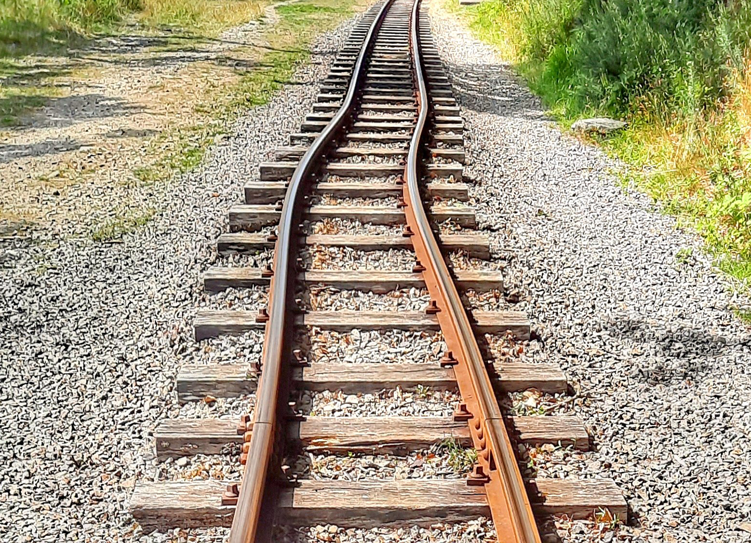 Railroad track with pronounced curve running through gravel and grassy surroundings