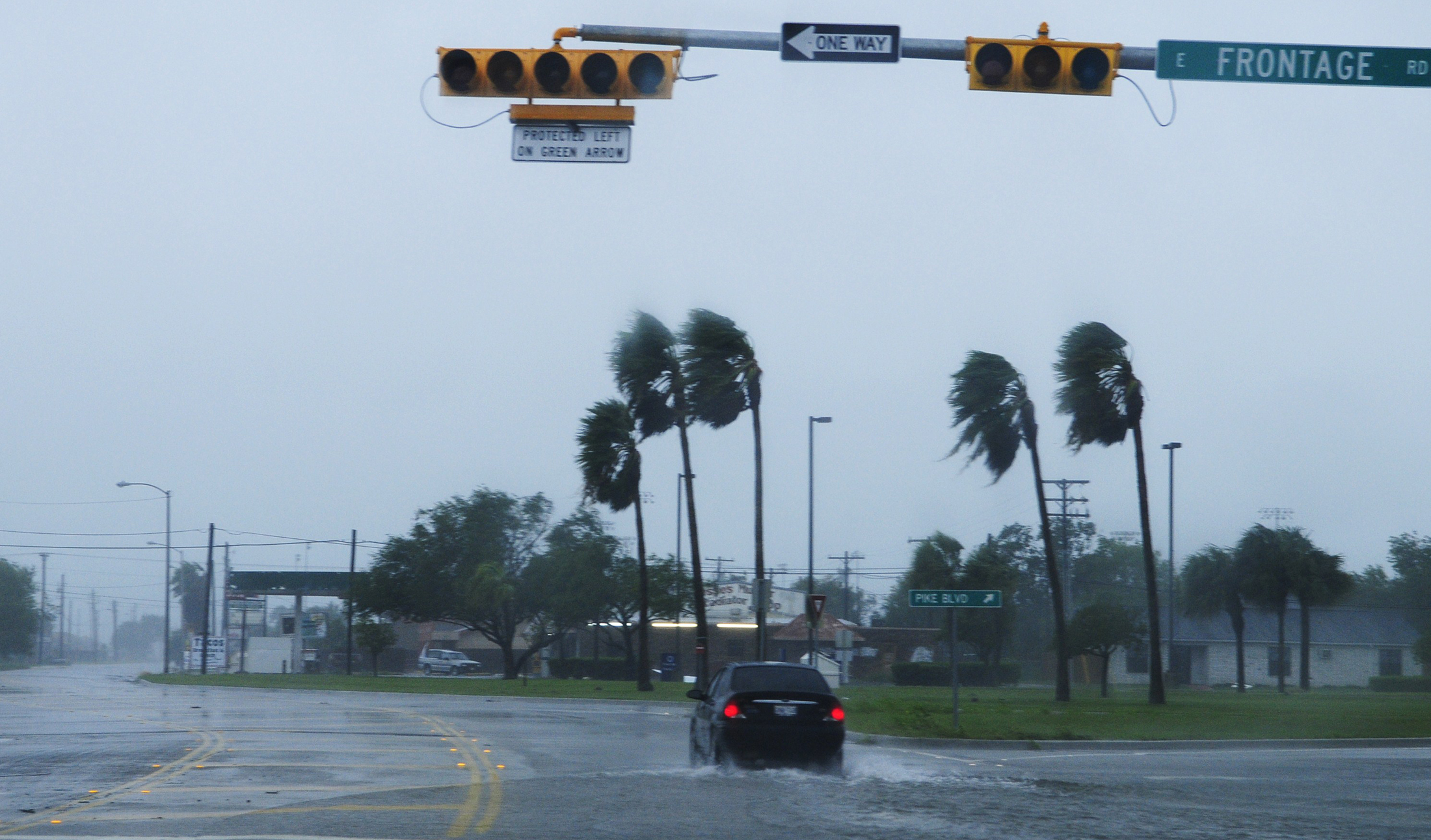 Car drives through flooded intersection as strong winds bend palm trees