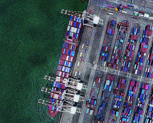 Aerial view of a cargo ship docked at a busy port full of colorful shipping containers. Gantry cranes are ready to load and unload cargo.