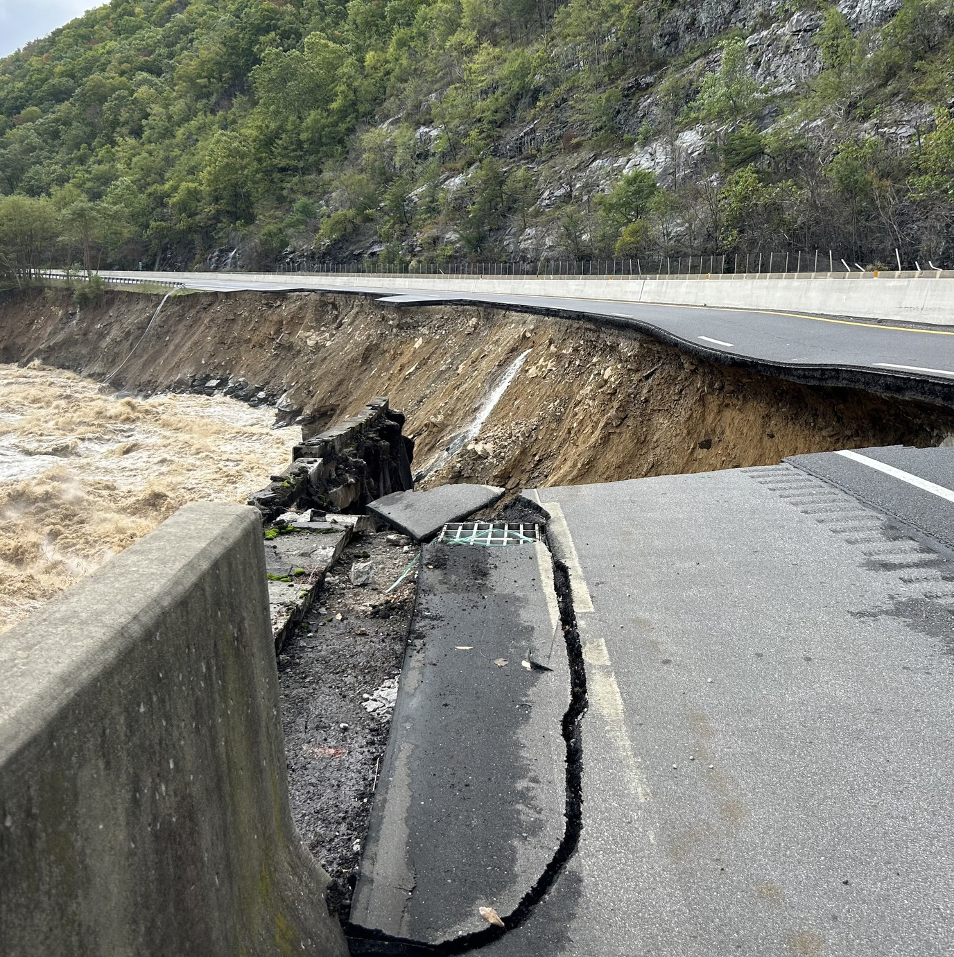 Collapsed highway lanes washed away by a rushing, muddy river next to a steep cliff