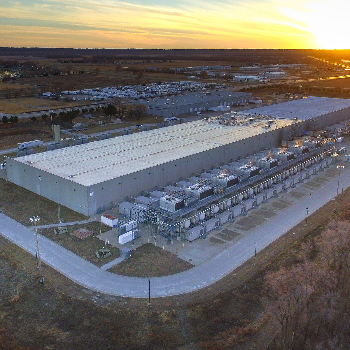Large industrial data center with cooling units beside lake at sunset
