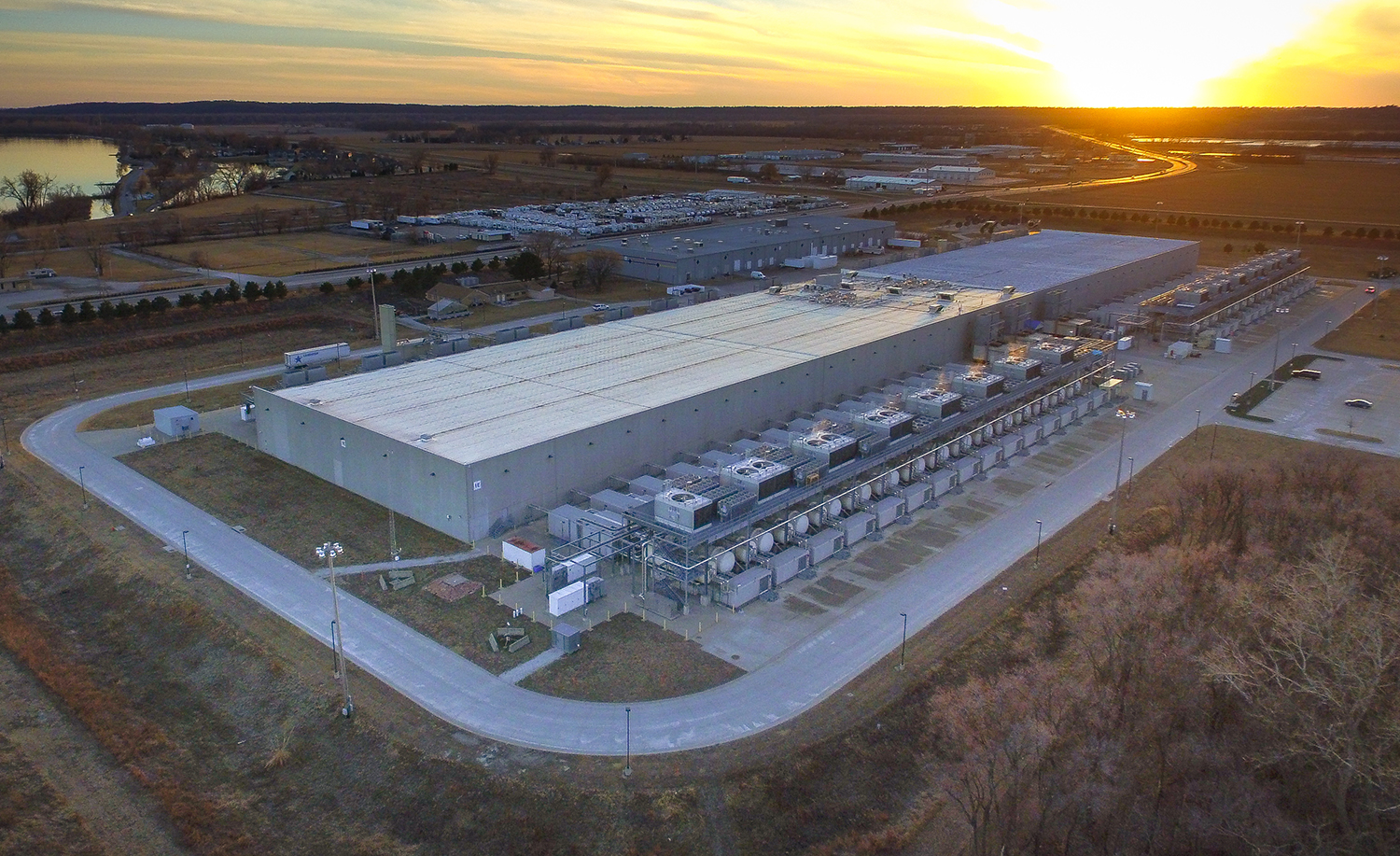 Large industrial data center with cooling units beside lake at sunset
