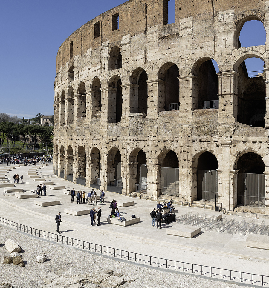 Colosseum exterior with restored plaza, visitors, and seating blocks underneath arches