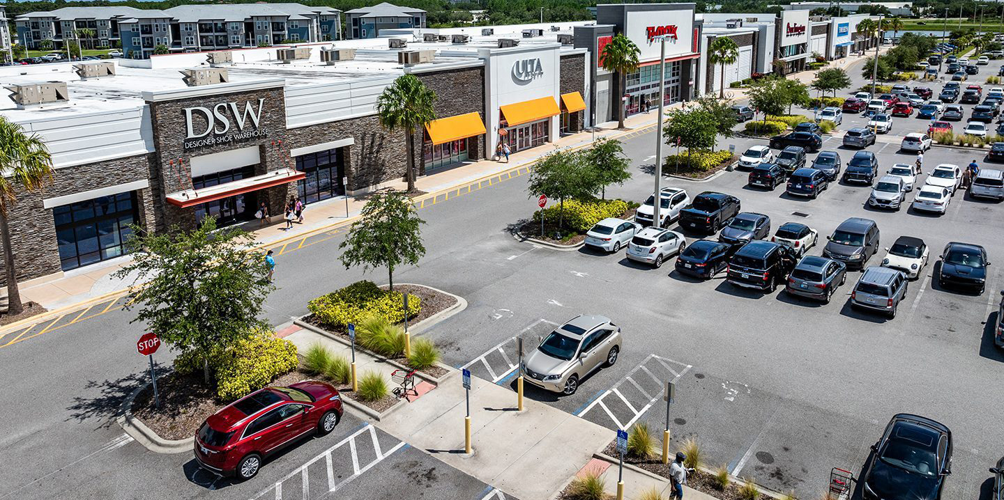 Aerial view of busy shopping center with storefronts, parking lot, and traffic