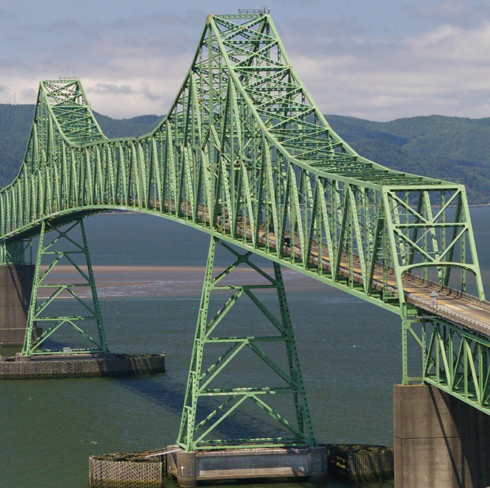Large green steel truss bridge spanning river with vehicles crossing