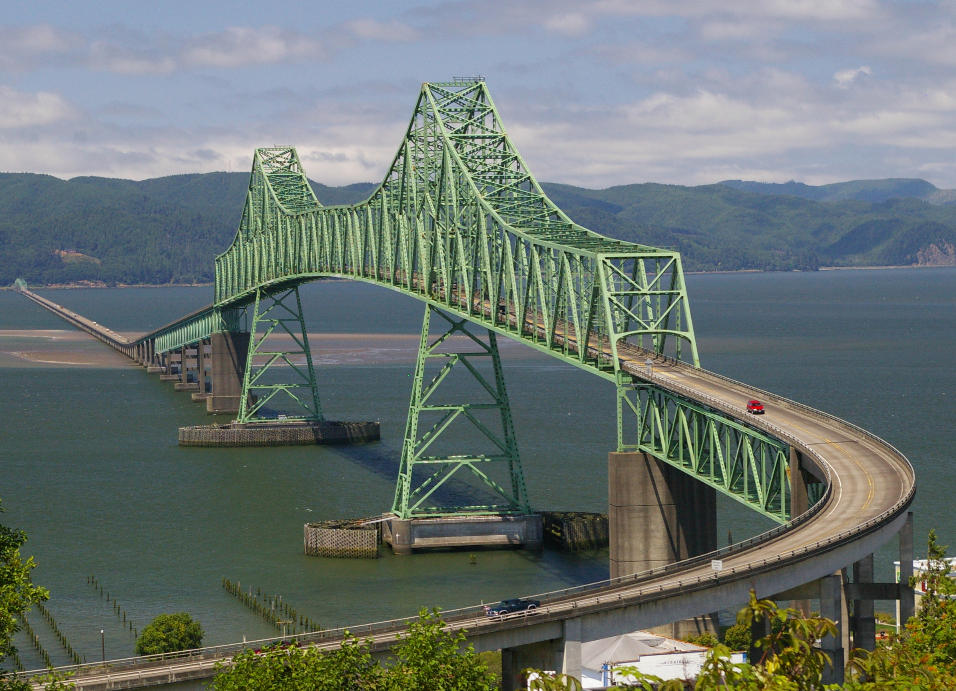 Large green steel truss bridge spanning river with vehicles crossing