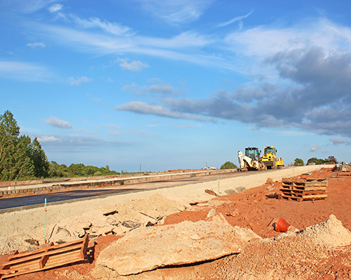 Construction site shows bulldozers and an unfinished road surrounded by clay