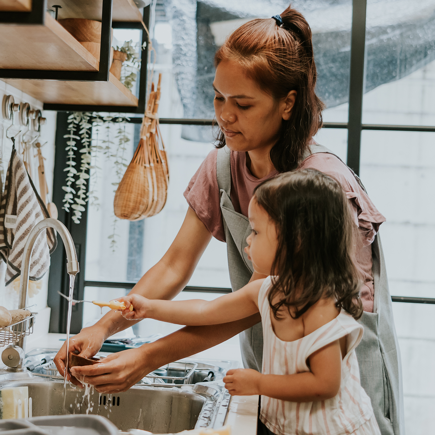 Person washing dishes at kitchen sink with a child nearby