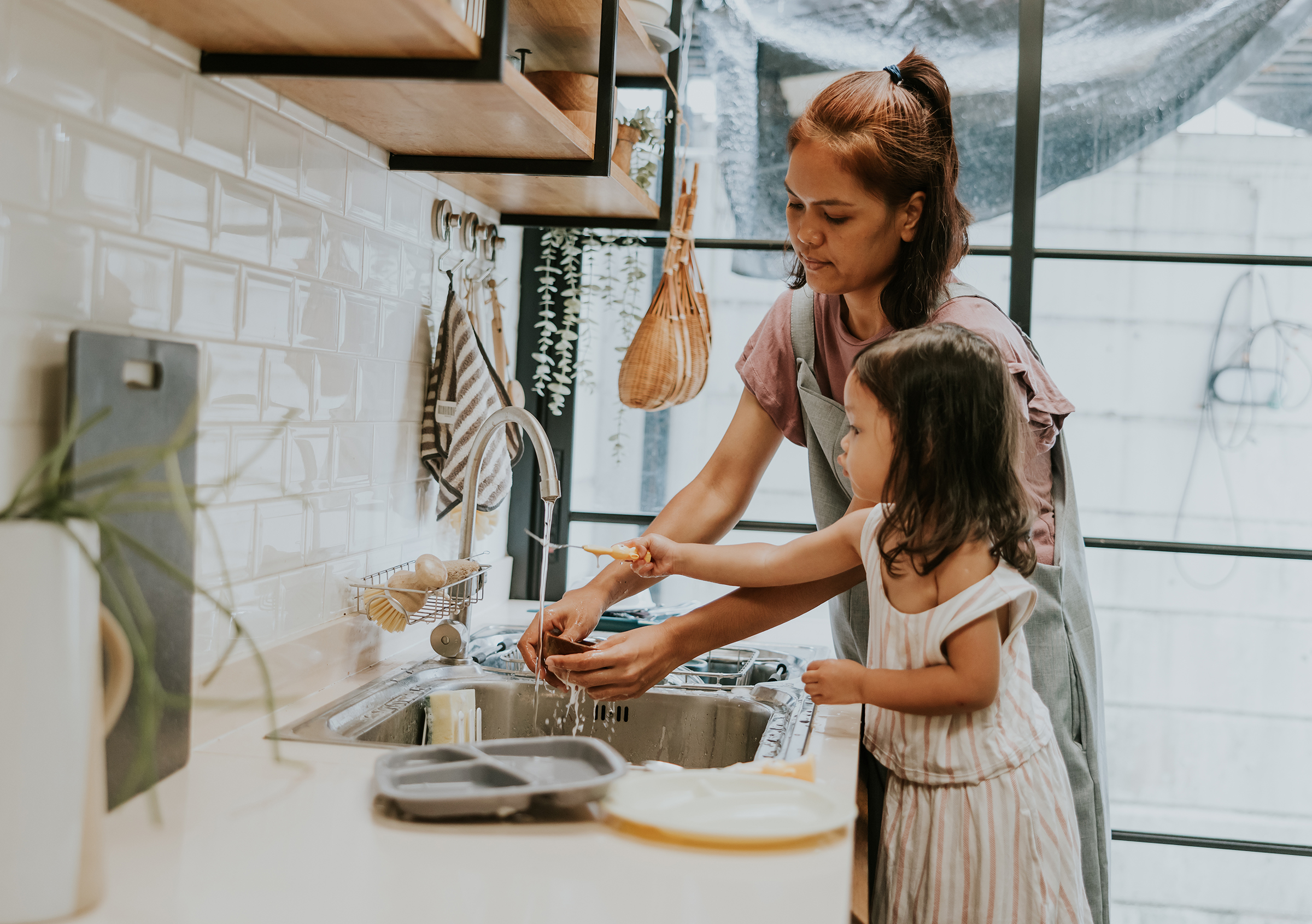 Person washing dishes at kitchen sink with a child nearby