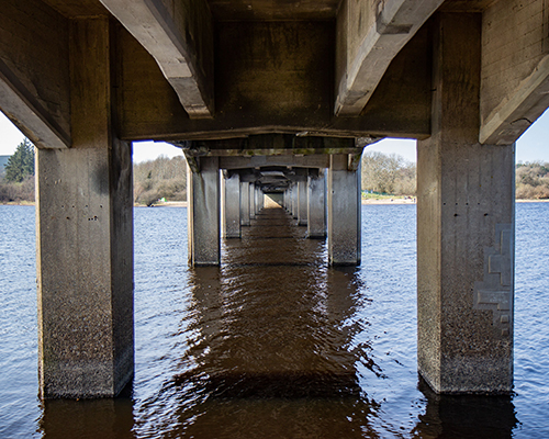 A low angle shot shows concrete bridge piers extending into a body of water