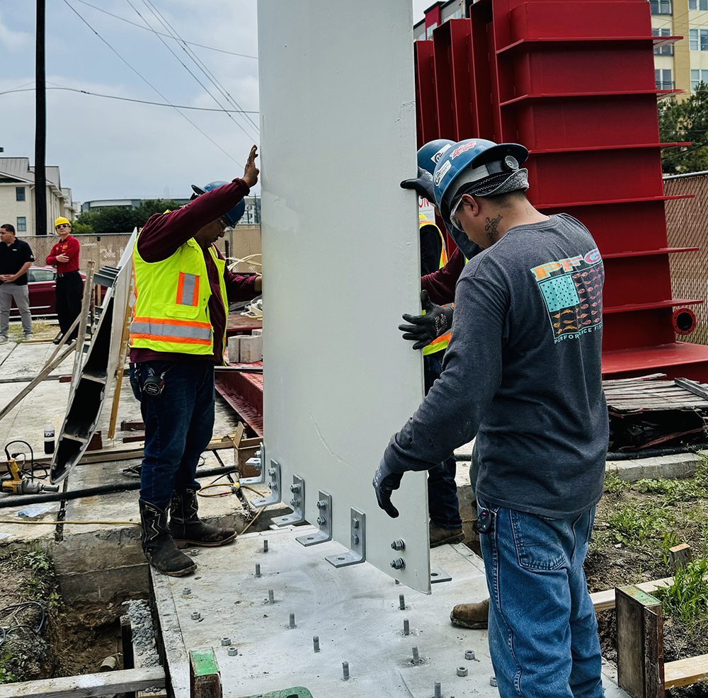 Workers install repurposed wind turbine blade segment on concrete foundation