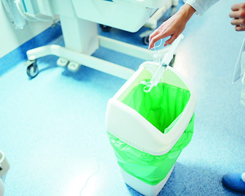 person in white coat tosses used syringe into white trash bin with green liner