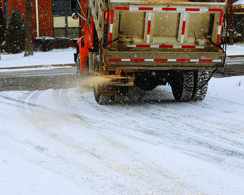 Orange dump truck spraying deicer on snowy street