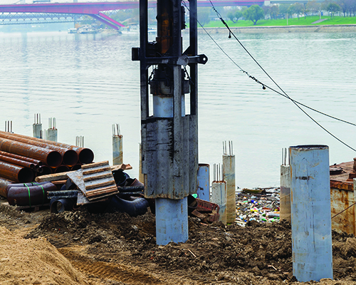 A pile driver at a construction scene along a riverbank