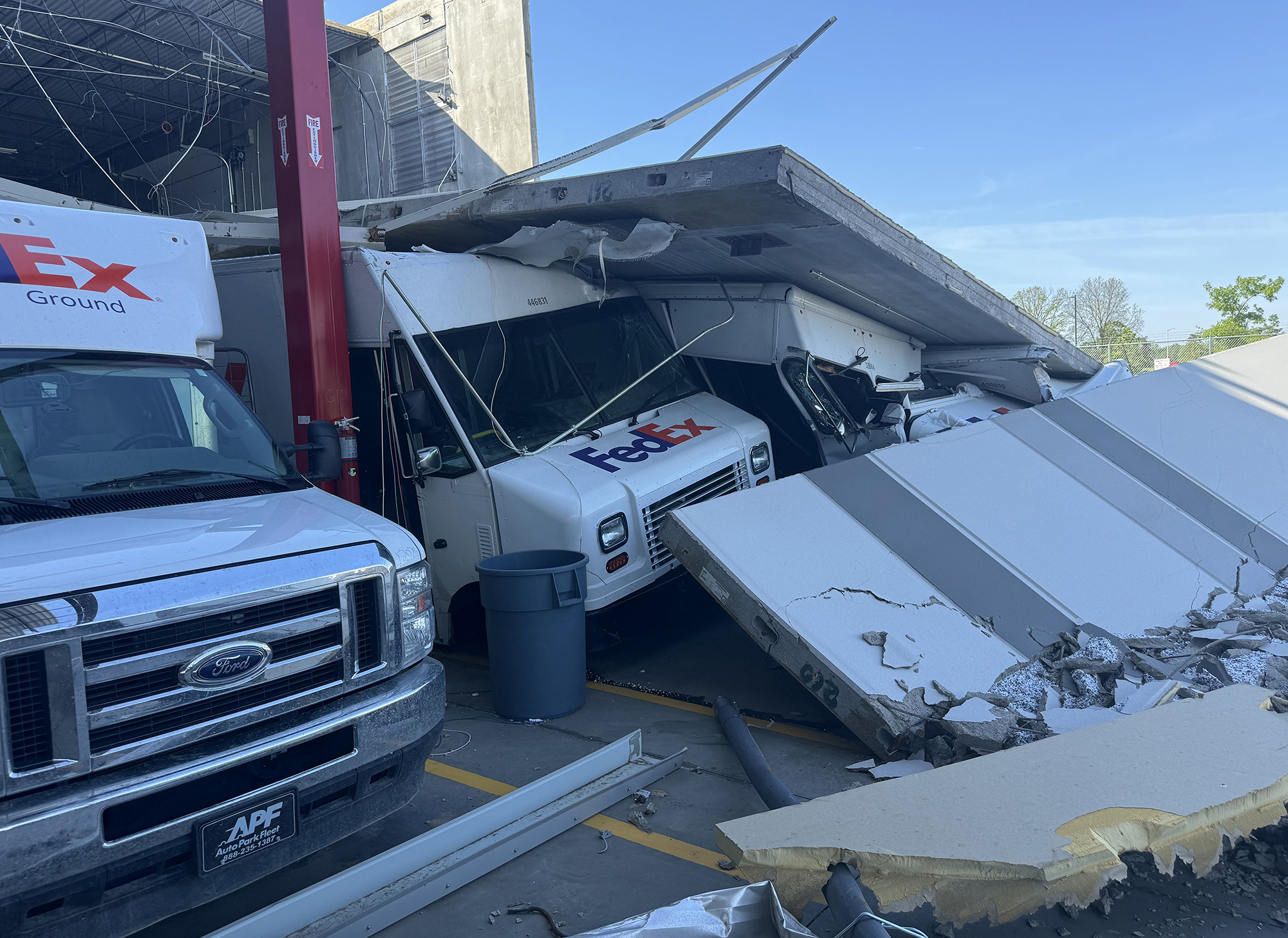 Collapsed wall panel damaged FedEx trucks at warehouse loading area.