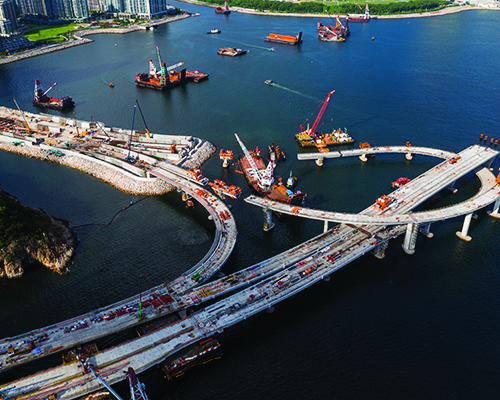 Eye-level aerial photo showing a bridge under construction over water with large construction cranes present
